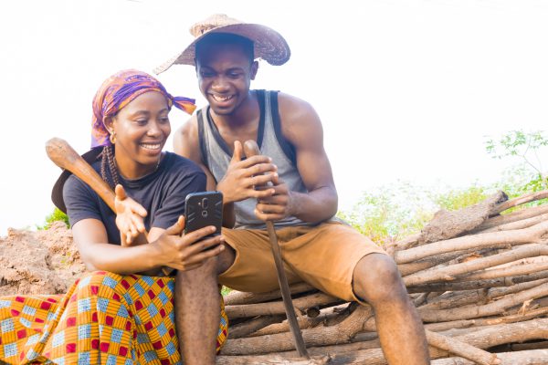 excited african couple doing internet banking on their farmland. male and female farmers using smartphone