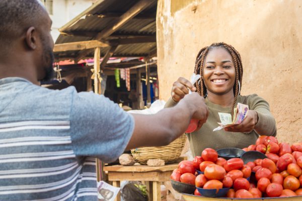 black girl selling tomatoes in a local african market to a male customer smiling and feeling happy and satisfied
